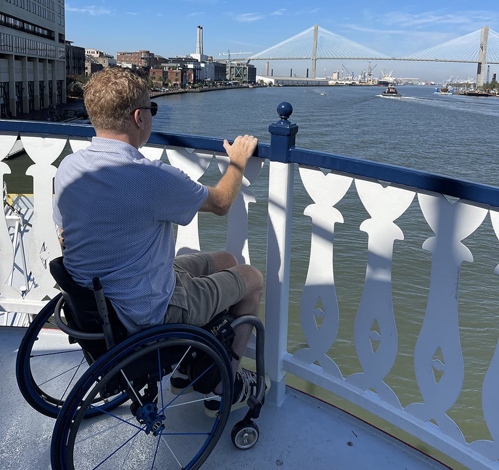 man in wheelchair looking over riverboat railing at water 
