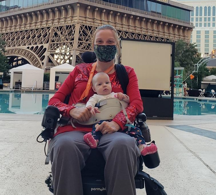 masked mother in wheelchair holding a baby on her lap