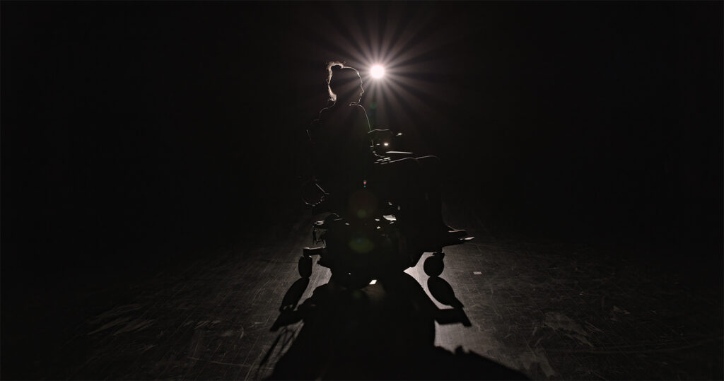 backlight woman in powerchair on dark stage