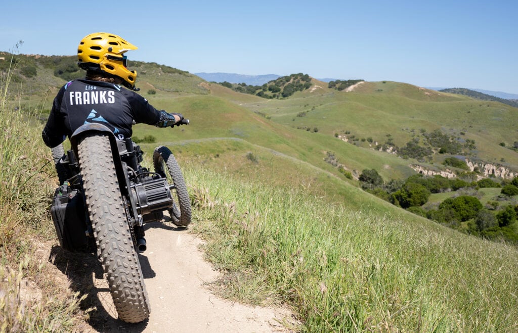 Lisa Franks riding mountain bike at the top of a hill with scenic mountain background