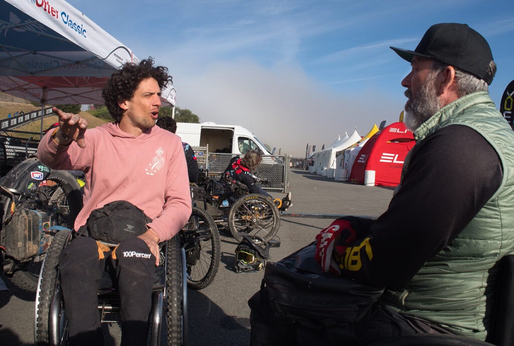 two men in wheelchairs in conversation with mountain bikers in background