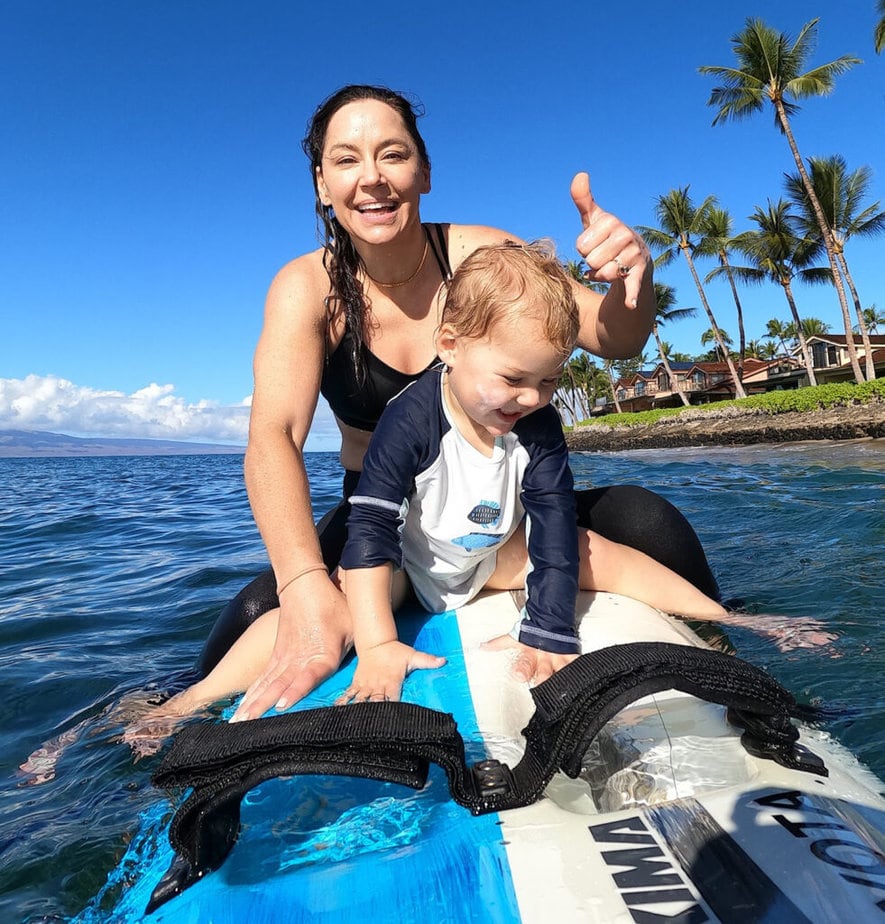 Woman out on the water sitting on a board with young child seated in front of her