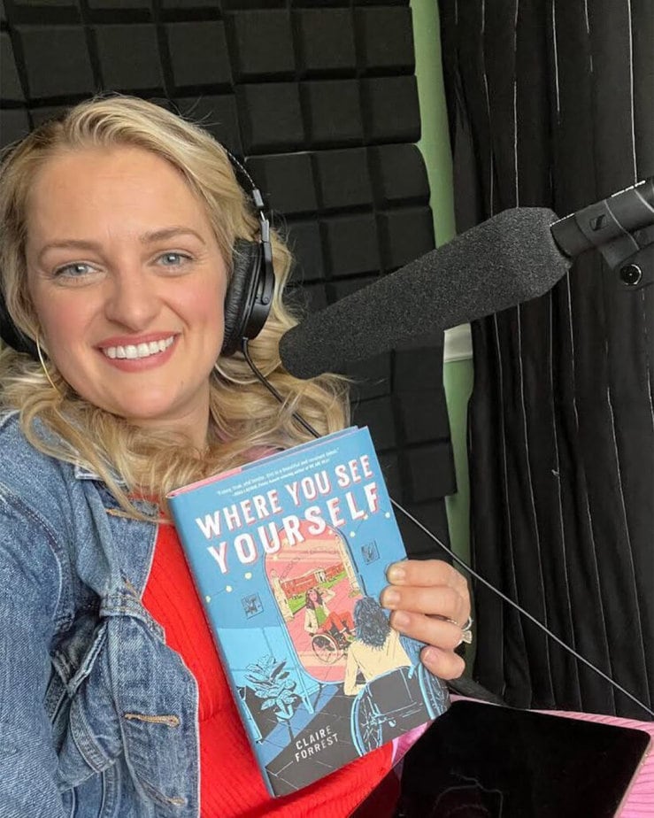 Ali Stroker wearing headset and holding up a book in front of microphone