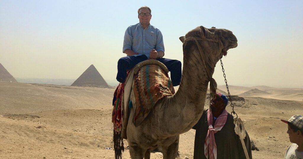 man seating on a camel with pyramids in the background