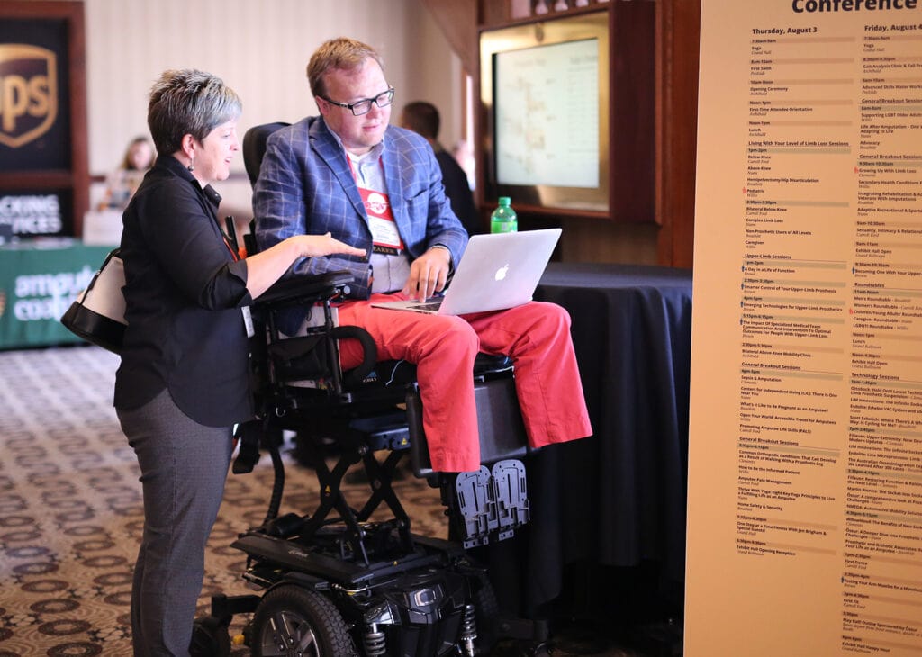 Woman standing next to man in powerchair in a convention hall