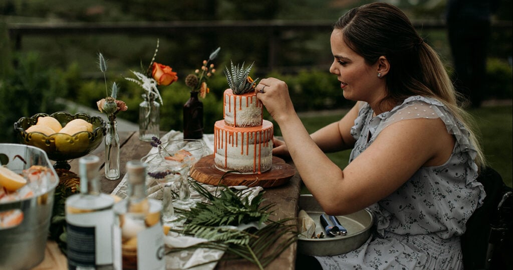 Woman sitting at a table outdoors decorating a cake