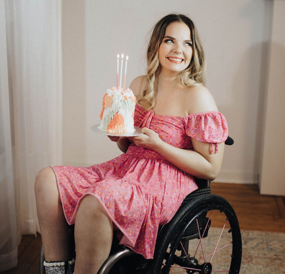 woman wearing pink dress sitting in wheelchair holding a decorated cake