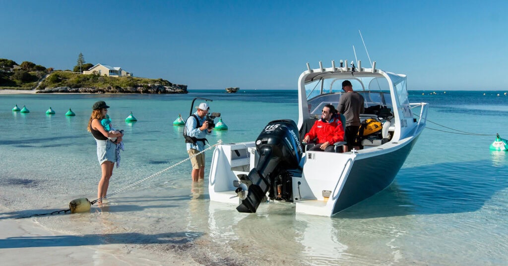 cameraman standing in surf filming people on boat anchored on beach