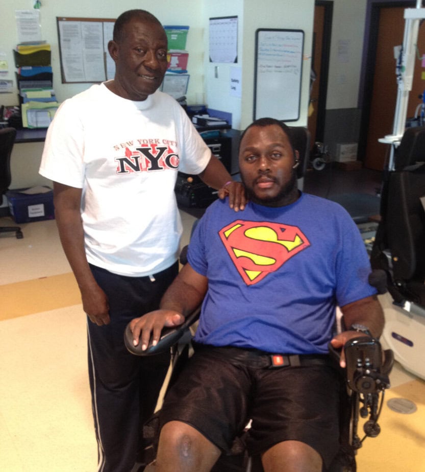 man standing next to man in power wheelchair wearing superman tee shirt
