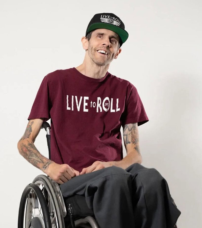 Man in wheelchair wearing tee shirt reading "Live to Roll"