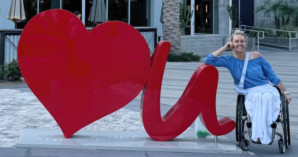 woman in wheelchair leaning elbow on sign smiling