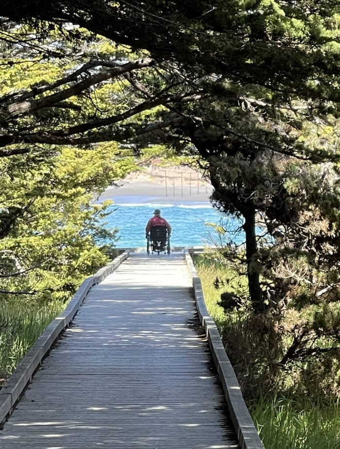 rear view of wheelchair user down a long path looking over the water