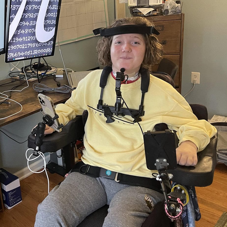 powerchair user wearing headset sitting in front of large computer screens