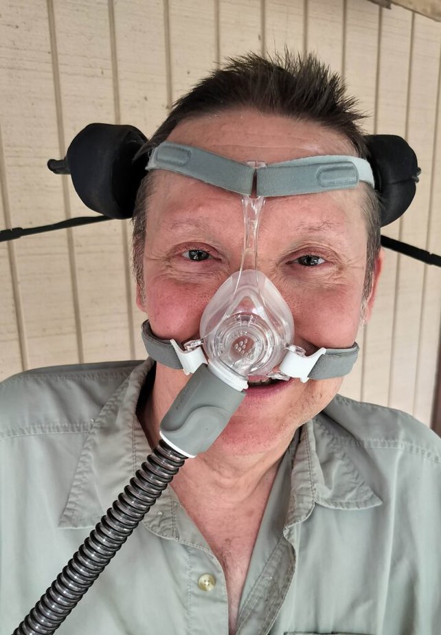 white man with a wheelchair headrest behind his head wearing a CPAP mask.