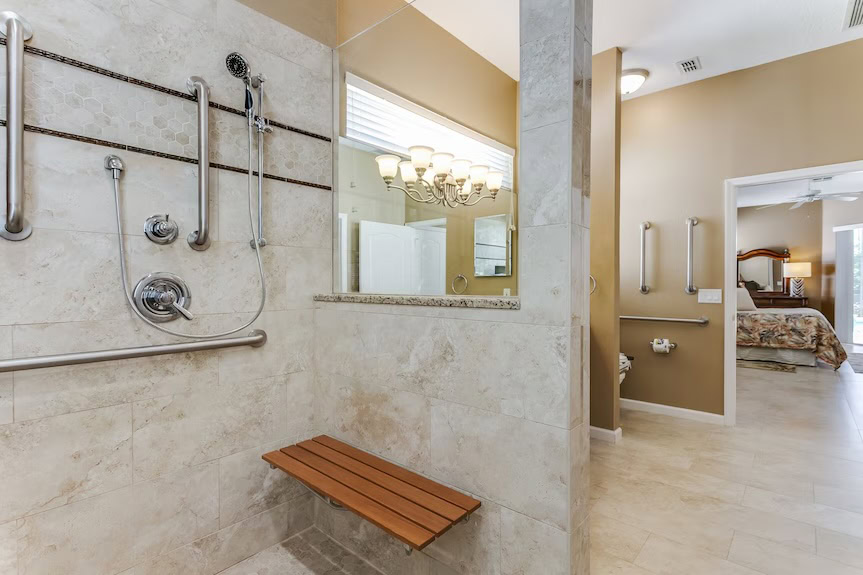 An accessible bathrom with a tiled roll-in shower and a wooden bench. 