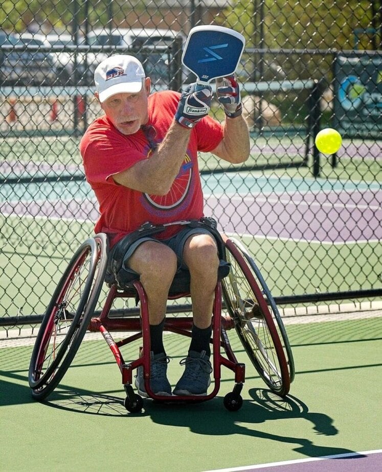 man in sport wheelchair taking a swing on a  paddleboard court