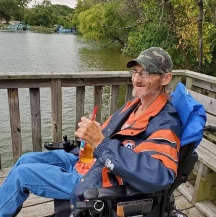 power wheelchair user sitting on a fishing dock holding a soda in his hand. 