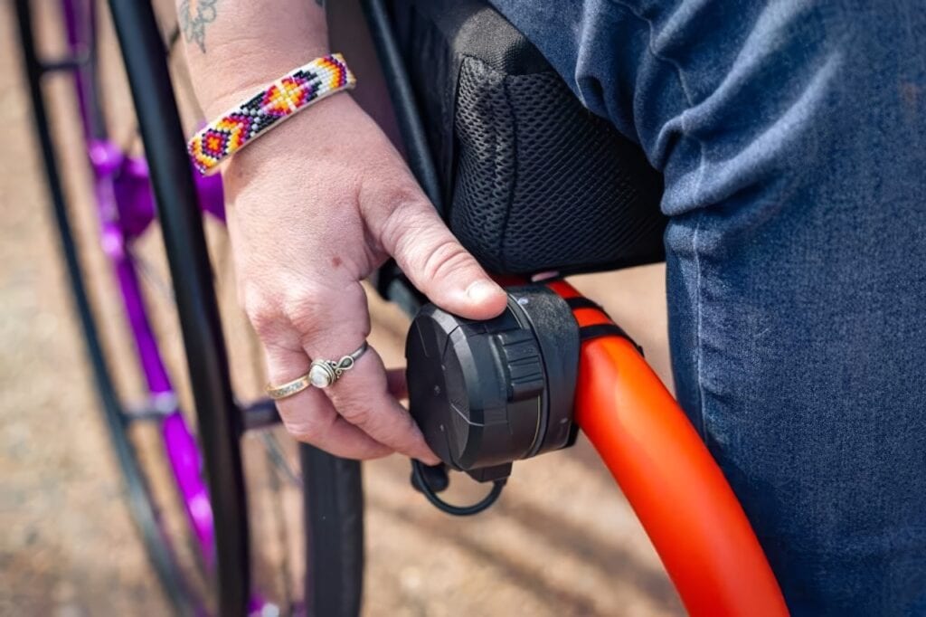 close up of a hand grasping a black dial attached to a manual wheelchair frame.  