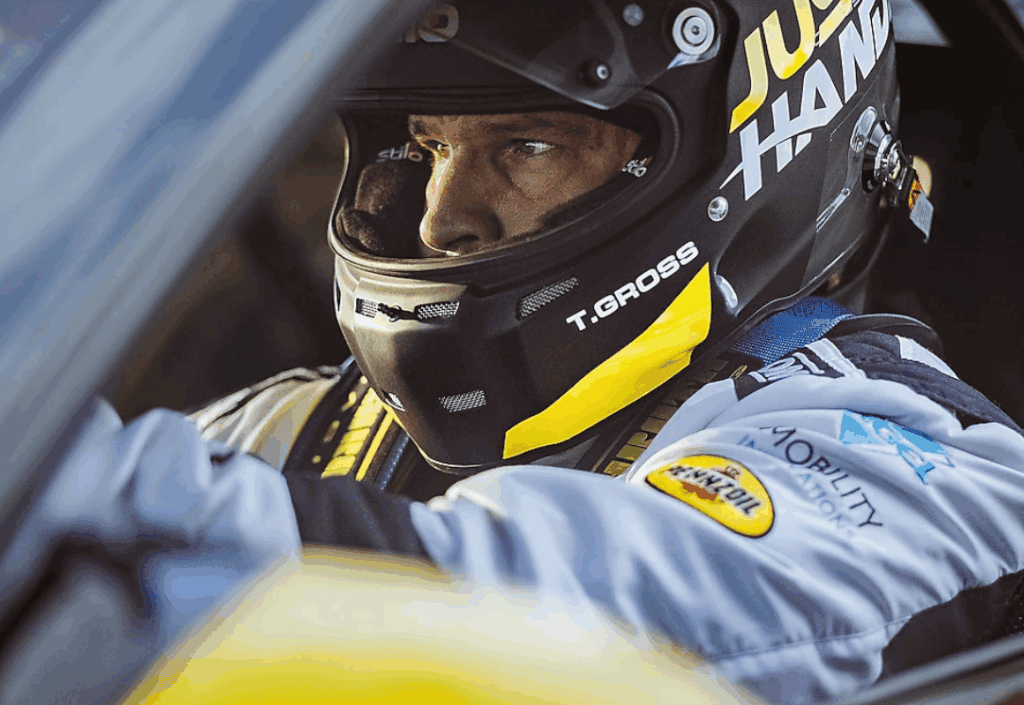close up of a man in a race car with crash helmet on. He is looking straight ahead with an intense look on his face.