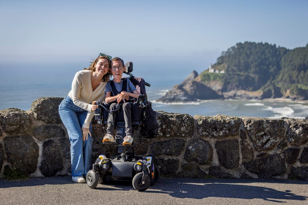 Man in power wheelchair on scenic coastal path with smiling woman