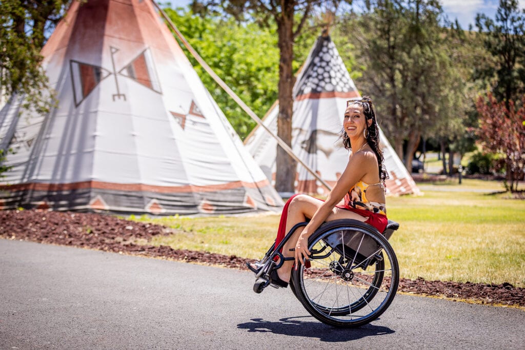 Young woman doing a wheelie in wheelchair in front of teepees.