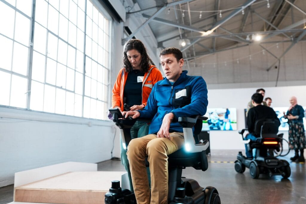 man using a Strutt ev1 power wheelchair in a warehouse.