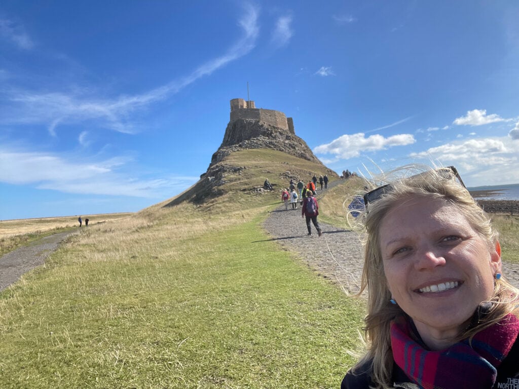 Scenic walk to ancient castle on grassy hill under bright blue sky.