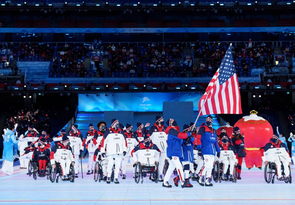 group of Team USA athletes, including wheelchair users at the front, march in the opening ceremonies parade.