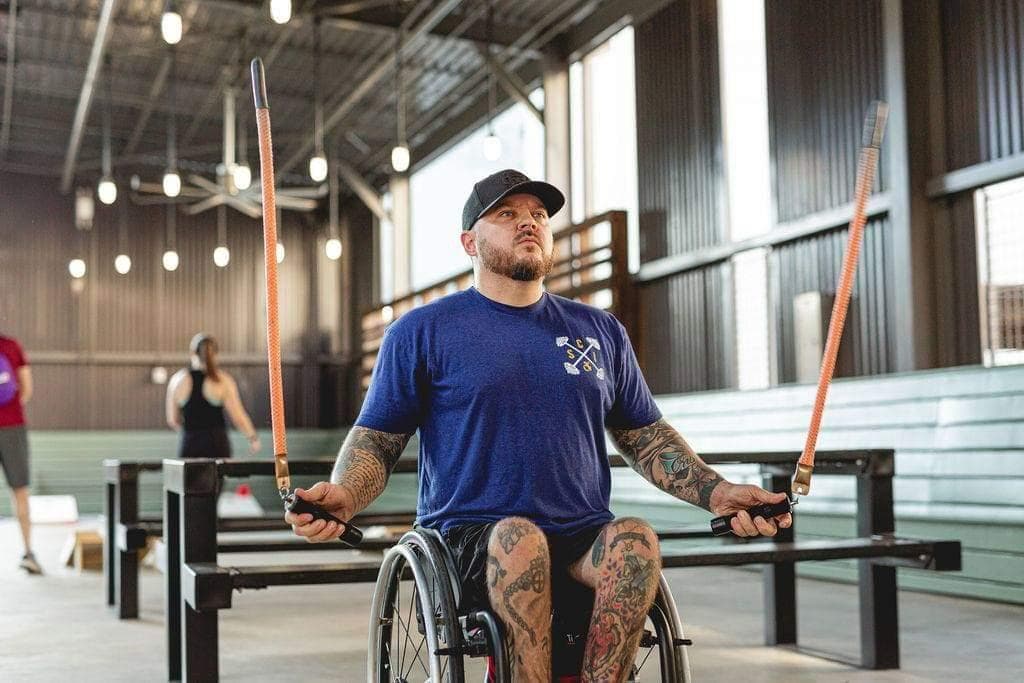 male manual wheelchair user in gym, swinging short jump ropes n each hand.