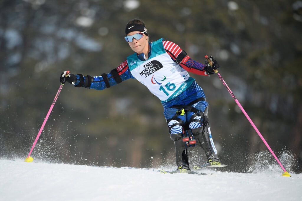 Woman competing on a cross-country sit ski, leaning into a turn. 