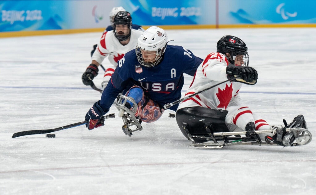 two sled hockey players battle for the puck on the ice. 