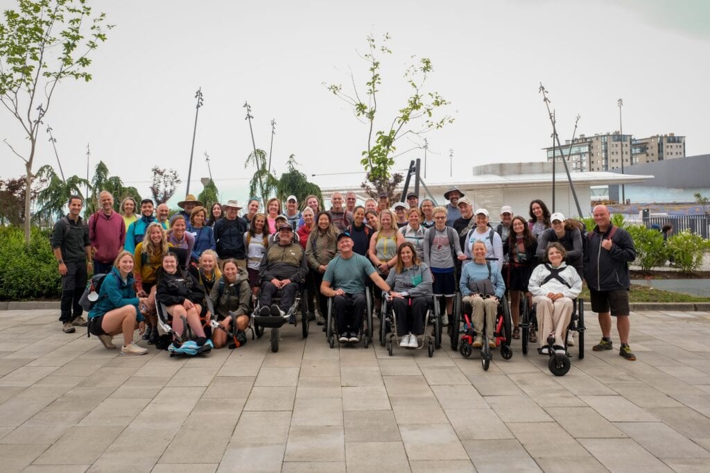 A group of people with several wheelchair users at the front pose outside.