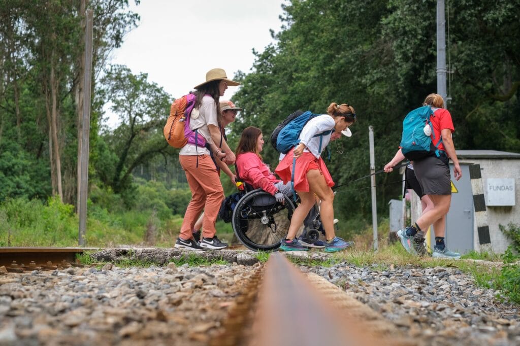 woman using manual wheelchair being helped across some railroad tracks. 