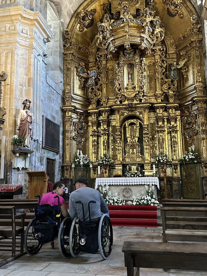 two manual wheelchair users seen from behind, facing an ornate church hall.
