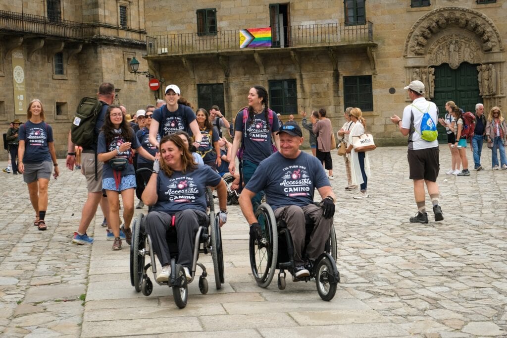 two wheelchair users with a group walking behind them in a town square.