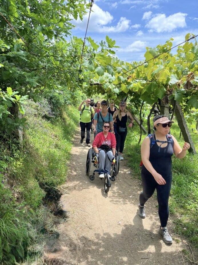 group of women, one using a manual wheelchair, on a path with grapevines surrounding it.