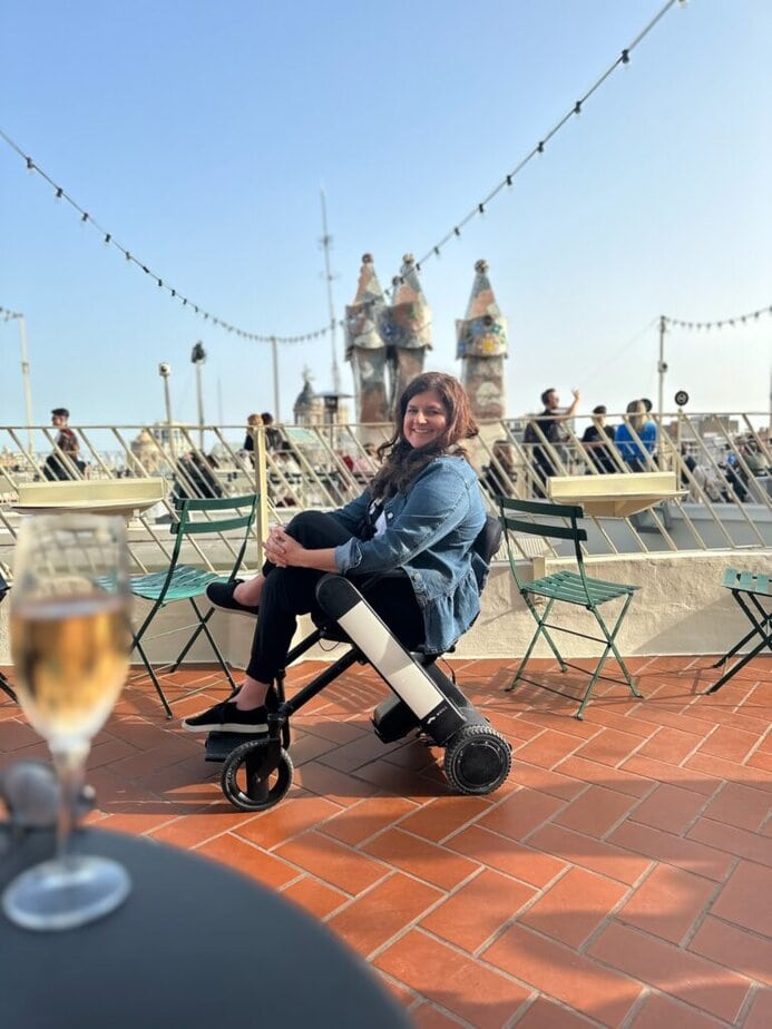 woman using Whill wheelchair in courtyard with Barcelona's Casa Batllo in background