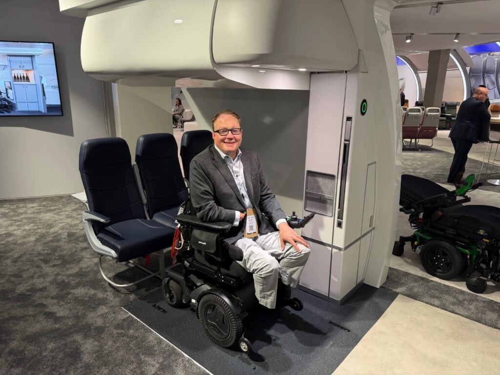 Man demonstrating sitting in his powerchair in a row of airline seats