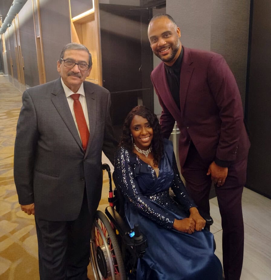 Woman in wheelchair with two men standing on either side, all smiling for camera