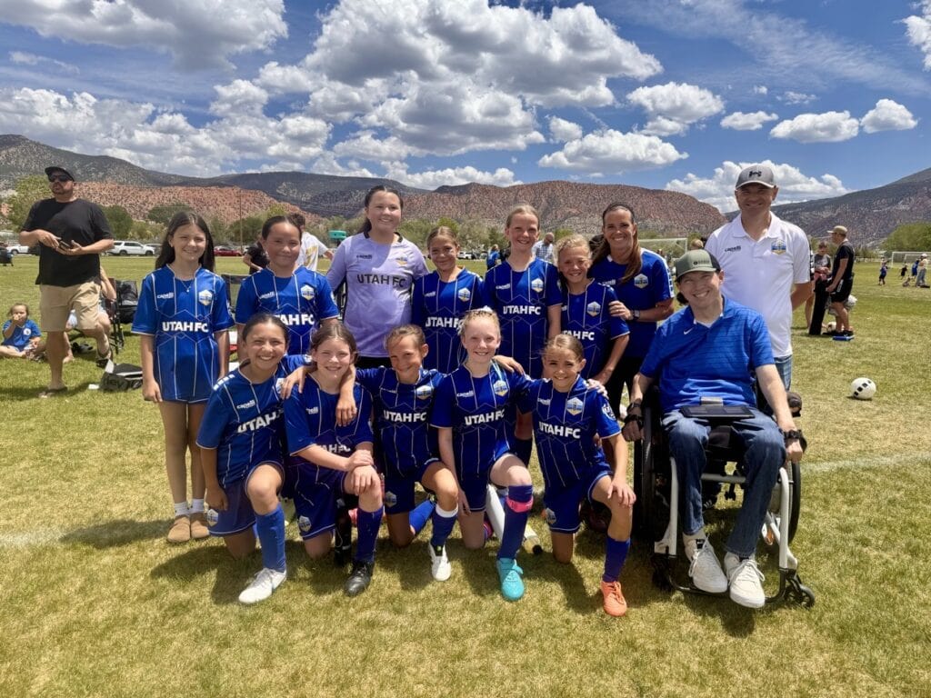 team photo of girls soccer team with two male coaches, one in a wheelchair