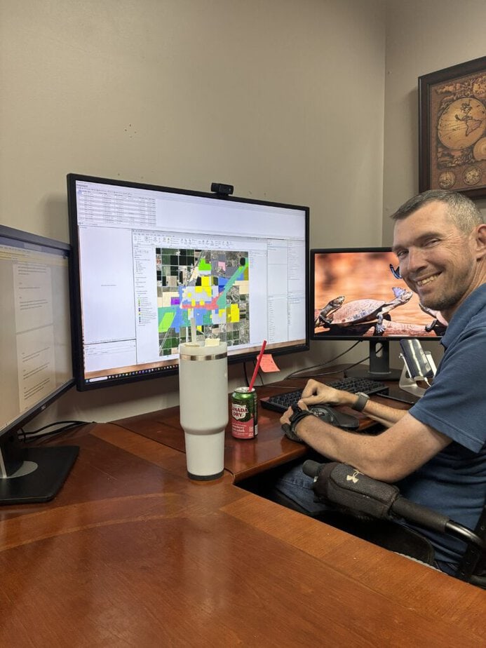man at a desk with one large computer screen and two smaller screens